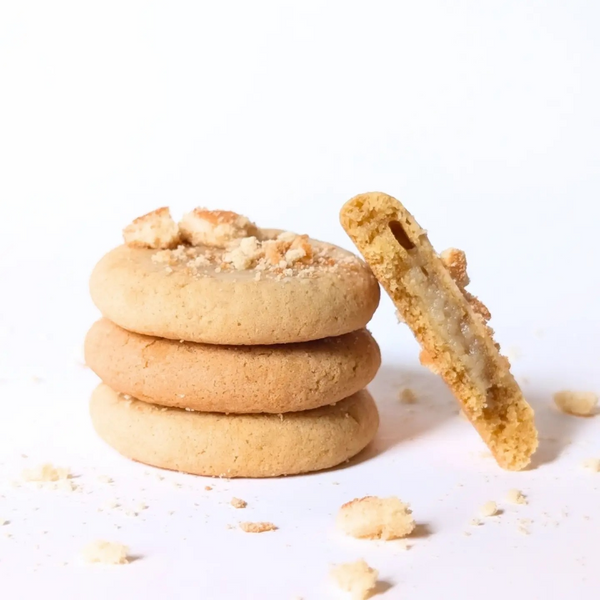 Three golden-brown cookies stacked on a white surface, with one cookie leaning against the stack and a crumb topping scattered around them.