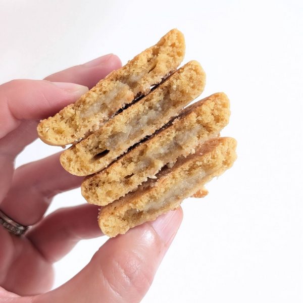 Four golden-brown cookies stacked and held between fingers against a plain white background.
