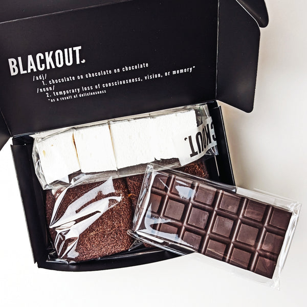 Open box of Blackout graham crackers and marshmallows, and a chocolate bar with a black lid displaying the brand name.
