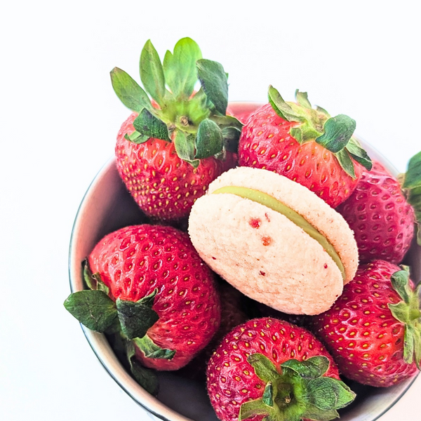 Strawberry matcha sandwich cookie in a bowl of strawberries on a white background