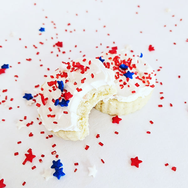 Cookie with white icing and red, white, and blue star sprinkles on a white background