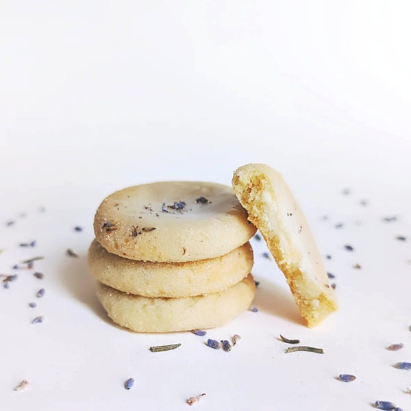 Blackout Baking Co. - Stack of lemon lavender cookies on a white surface with scattered lavender buds.